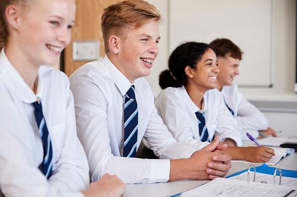 school students smiling whilst sitting working at desk